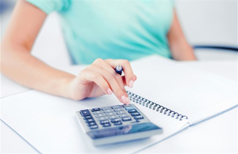 Person in green shirt using a calculator that is sitting on top of a notebook